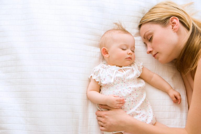 Mother and baby girl lying in bed and sleeping with the mother holding her baby